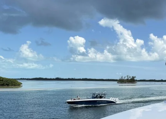 A small mangrove island across flat shallow water in the Florida Keys, with a boat running past under piled afternoon clouds